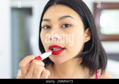 Primo piano ritratto di una donna biraciale mettendo su rossetto rosso, spazio copia. Concetto di tempo libero, festa e stile di vita. Foto Stock