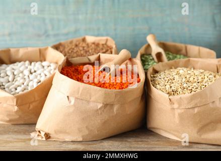 Grani e cereali diversi in sacchetti di carta su tavola di legno Foto Stock