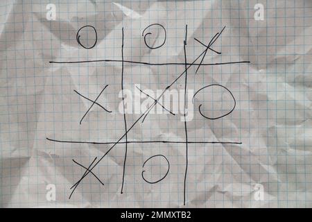 il gioco del tic-tac-toe è disegnato con una penna su un taccuino sbriciolato in una gabbia, gioco e riposo, gioco per bambini di tic-tac-toe Foto Stock