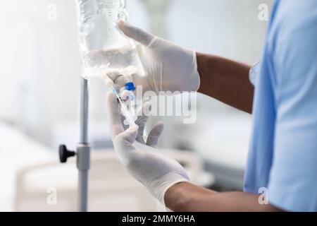 Primo piano di un medico afro-americano che lavora in ospedale, cambiando gocciolamento Foto Stock