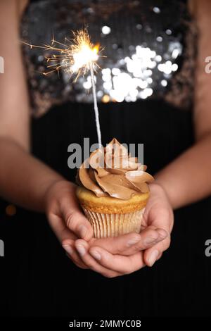 Donna che tiene cupcake di compleanno con scintilla, primo piano Foto Stock