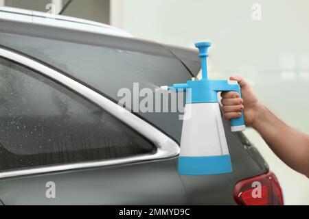 L'operatore spruzzerà acqua sul finestrino dell'auto prima di colorare in officina, in primo piano Foto Stock