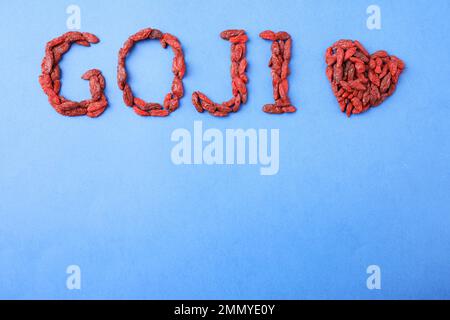 Parola GOJI e cuore fatto di bacche essiccate su fondo blu, piatto giacitura. Spazio per il testo Foto Stock