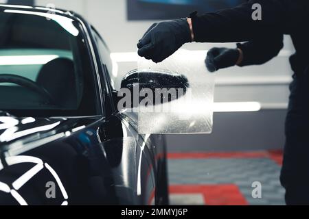 Procedura di installazione del PPF sullo specchietto laterale. Protezione anti-gravità. Lavoratore professionista maschio che applica PPF sullo specchio laterale. Foto di alta qualità Foto Stock