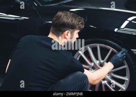 Uomo annerimento della ruota di pneumatico di auto utilizzando spugna con chimico annerimento di gomma nel dettaglio auto servizio. Vista posteriore. Foto di alta qualità Foto Stock