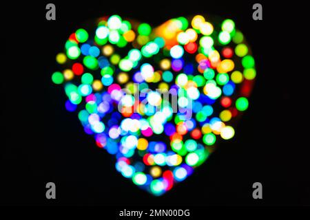 Arcobaleno confetti dalla luce con effetto bokeh a forma di cuore su sfondo nero (sfondo San Valentino) Foto Stock