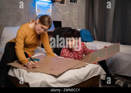 Attivisti donna e uomo pittura poster per segno di protesta per salvare il pianeta disegno cartellone in dormitorio studenti. Foto Stock