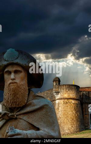 Francia, Pirenei Atlantici, Bearn, Navarrenx, scultura di un pellegrino sulla strada per San Giacomo di fronte ai bastioni di una città sotto un cielo tempestoso Foto Stock