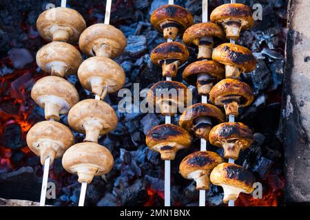 Il barbecue Shampynon è fritto su carbone. Preparazione di funghi alla griglia su spiedini, crudi e pronti. Cibo sul fuoco. Foto di alta qualità Foto Stock