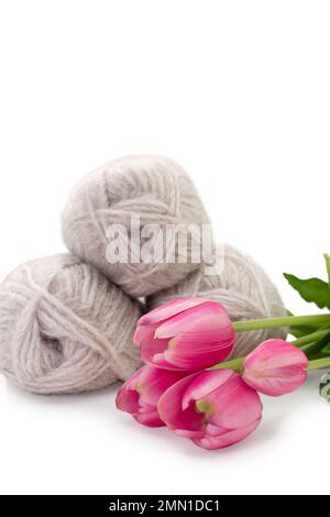Gruppo di lana grigia di filato e filo con tulipano rosa su fondo bianco isolato. Maglieria, hobby, inverno. Spazio di copia. Vista laterale. Donne internazionali Foto Stock
