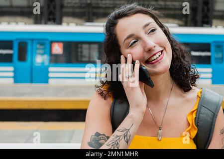 Bella giovane donna argentina sorridente e parlando al telefono dicendo Arrivederci a sua madre, in attesa che il treno a bordo e andare in un viaggio attraverso Foto Stock