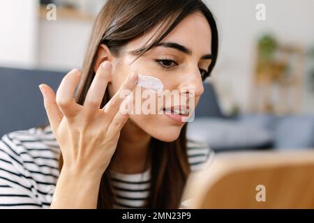 Giovane donna che usa prodotti per la cura della pelle. Donna che prende la crema per applicare sulla pelle del viso Foto Stock