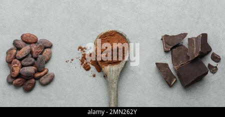 Cucchiaio di cacao, cioccolato fondente e cacao in grani su fondo grigio in cemento Foto Stock