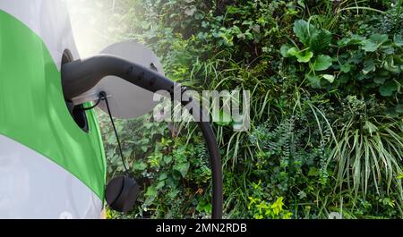 Primo piano di un'auto elettrica con cavo di ricarica sullo sfondo di una parete verde con giardino verticale Foto Stock