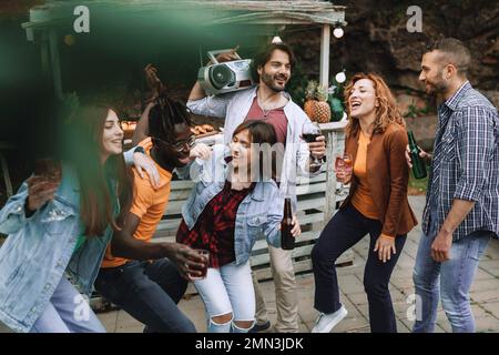 Un gruppo di amici ama ballare e bere birre, cocktail e vino presso il bar sulla spiaggia. Uno di loro tiene un bossolo sulla spalla. Un ma africano Foto Stock