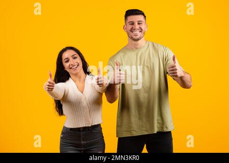 Allegro eccitato giovane coppia araba in casual mostrando pollici fino segno con le mani, raccomandare la vendita Foto Stock