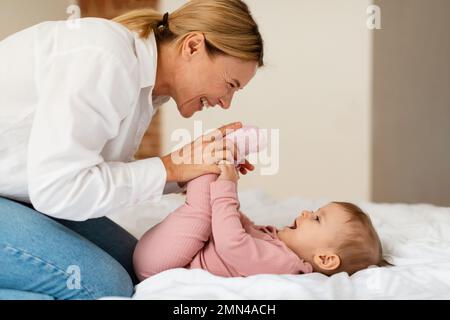 Assistenza ai bambini. Donna felice che fa ginnastica alla sua bambina, giocando e legandosi con il bambino, godendo il tempo insieme Foto Stock