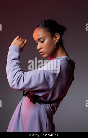 bruna donna afroamericana in felpa e gilet in posa grigio e viola Foto Stock