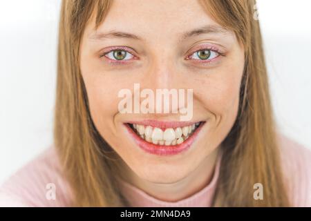 Primo piano volto di donna caucasica con ampio sorriso toothy e occhi verdi guardando la macchina fotografica. Foto di alta qualità Foto Stock