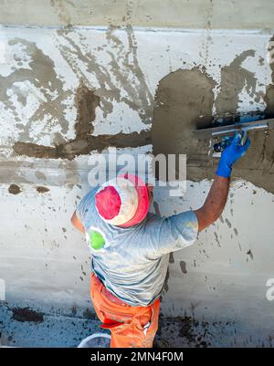 Lavoratore di costruzione che sparge Malta tixotropica su parete di calcestruzzo con lesioni strutturali Foto Stock