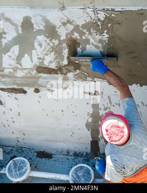 Lavoratore di costruzione che sparge Malta tixotropica su parete di calcestruzzo con lesioni strutturali Foto Stock