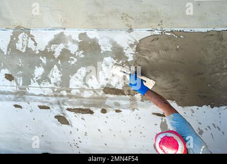 Lavoratore di costruzione che sparge Malta tixotropica su parete di calcestruzzo con lesioni strutturali Foto Stock