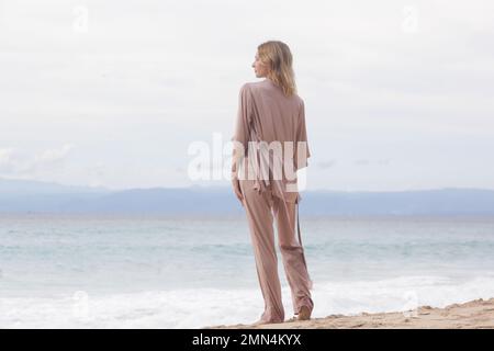 Ritratto di bella giovane donna in seta beige vestito su spiaggia di sabbia vuota, idilliaca vacanza estiva lontano dalla città Foto Stock