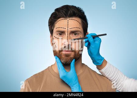 Chirurgo plastico disegnare segni sul viso dell'uomo per l'operazione di chirurgia estetica, bell'uomo in posa su sfondo blu Foto Stock