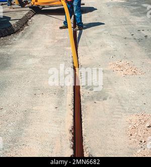 Il lavoratore inserisce cavi in fibra ottica interrati in una micro trincea Foto Stock