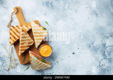 Quattro panini fatti in casa con salsiccia, formaggio e rucola su un fondo di cemento chiaro. Il concetto di un pasto veloce o uno spuntino al lavoro o a scuola. In alto Foto Stock