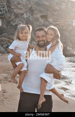 Amore e cura di papà. Il padre tiene in braccio due figlie, forza e coraggio. Famiglia amichevole a casa e in vacanza. Foto Stock