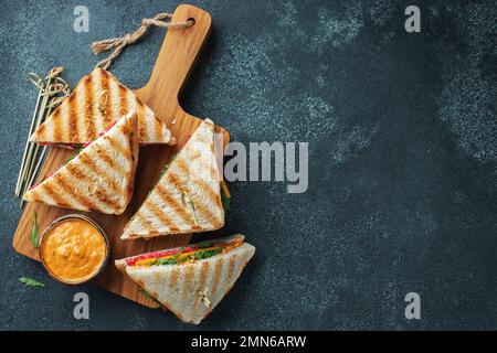 Quattro panini fatti in casa con salsiccia, formaggio e rucola su fondo di cemento scuro. Il concetto di un pasto veloce o uno spuntino al lavoro o a scuola. Parte superiore v Foto Stock