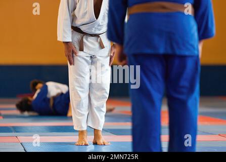 Due combattenti di judo o atleti si salutano a vicenda in un arco prima di praticare le arti marziali sullo sfondo della partita in corso Foto Stock