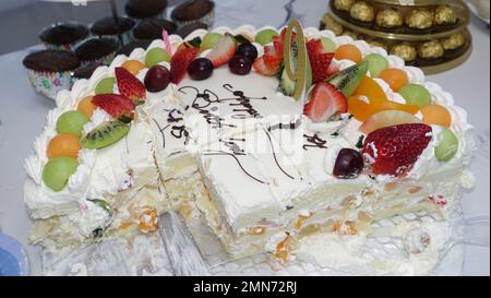 Mezza torta di frutta sul tavolo con altro dessert per la celebrazione del compleanno Foto Stock