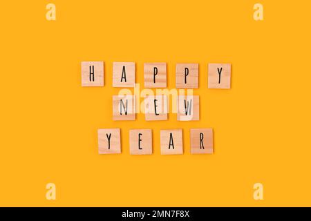 Felice Anno Nuovo. Citazione fatta di blocchi di legno con lettere su sfondo giallo. Foto Stock