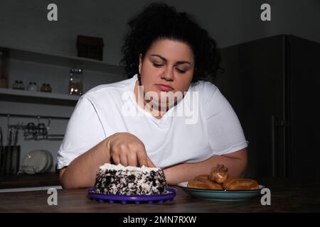 Donna in sovrappeso depressa che mangia torta in cucina di notte Foto Stock