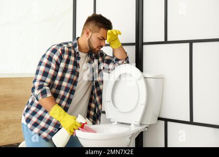 Giovane uomo che sente disgusto mentre pulisce il water ciotola in bagno Foto Stock