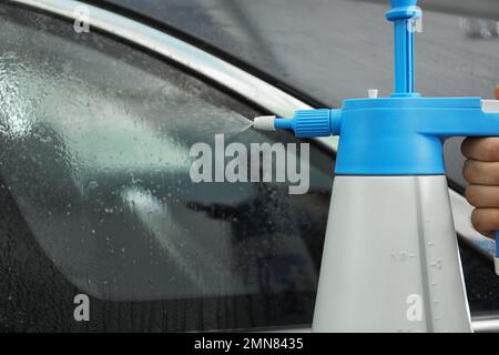 L'operatore spruzzerà acqua sul finestrino dell'auto prima di colorare in officina, in primo piano Foto Stock