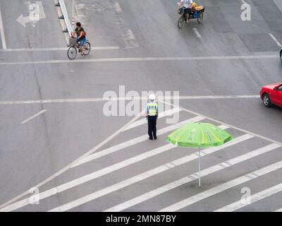 Un po' isolato e forse solitario poliziotto ufficiale del traffico ad un incrocio stradale nella città cinese di Xi'an. PRC. Cina. Guidare e dirigere una piccola quantità di traffico ma guardando esposto. Ha un grande ombrellone per l'ombra se ne ha bisogno. (125) Foto Stock