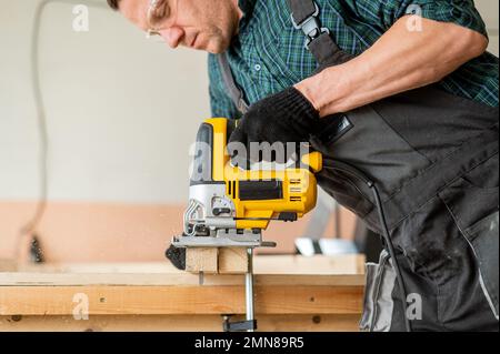 Un uomo taglia una tavola di legno con un seghetto elettrico in un'officina  Foto stock - Alamy