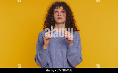 Donna esausta con capelli ricci stanchi toglie gli occhiali, sente dolore agli occhi, essendo burnout overwork da lunghe ore di lavoro, mal di testa. Infelice ragazza adolescente triste isolato da solo su sfondo giallo studio Foto Stock