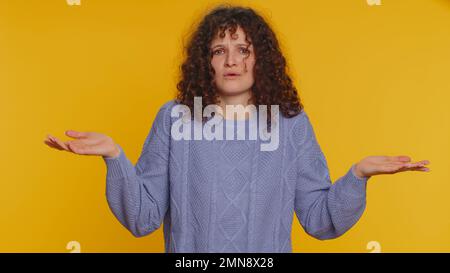 Non so cosa dire. Donna confusa che si sente imbarazzata circa la domanda ambigua, avendo dubbi, nessuna idea, essendo clueless ed incerto. Giovane ragazza dai capelli ricci isolata su sfondo giallo studio Foto Stock