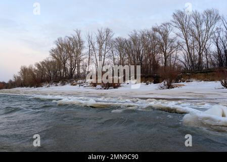Il primo debole ghiaccio autunnale sorge in onde dal flusso d'acqua vicino alla riva della foresta. Foto Stock
