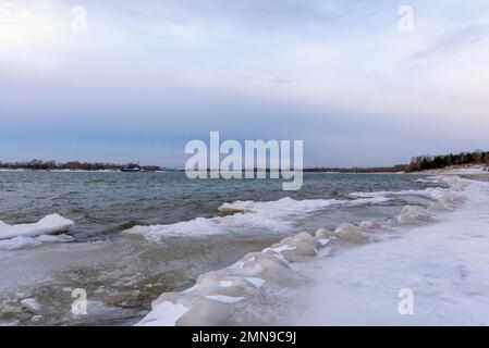 Il primo debole ghiaccio autunnale sorge in onde da una forte corrente d'acqua vicino alla riva della foresta. Foto Stock
