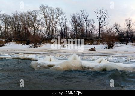 Il primo debole ghiaccio autunnale sorge in onde dalla forte corrente e dal vento dell'acqua vicino alla riva della foresta. Foto Stock