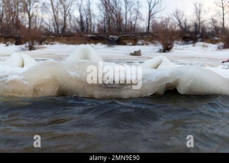 Il primo debole ghiaccio autunnale sorge in onde da una forte corrente e vento d'acqua vicino alla costa con alberi forestali. Foto Stock