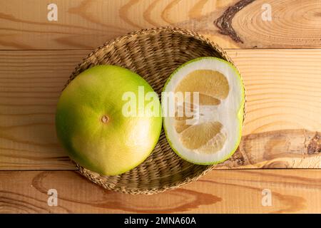 Un intero e mezzo succosa dolcetto di agrume organico in un piatto di paglia, primo piano, su un tavolo di legno, vista dall'alto. Foto Stock