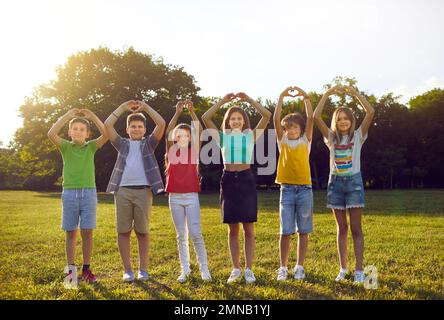 Ritratto di gruppo di bambini felici e sorridenti in piedi nel parco e facendo gesti di cuore Foto Stock