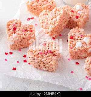 Krispie di riso rosa a forma di cuore per San Valentino con spolverini di cuore rosso serviti con latte Foto Stock