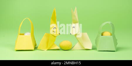 Origami di Pasqua - due coniglietti di carta e un uovo, sfondo verde. Artigianato per le vacanze, fatelo da soli Foto Stock